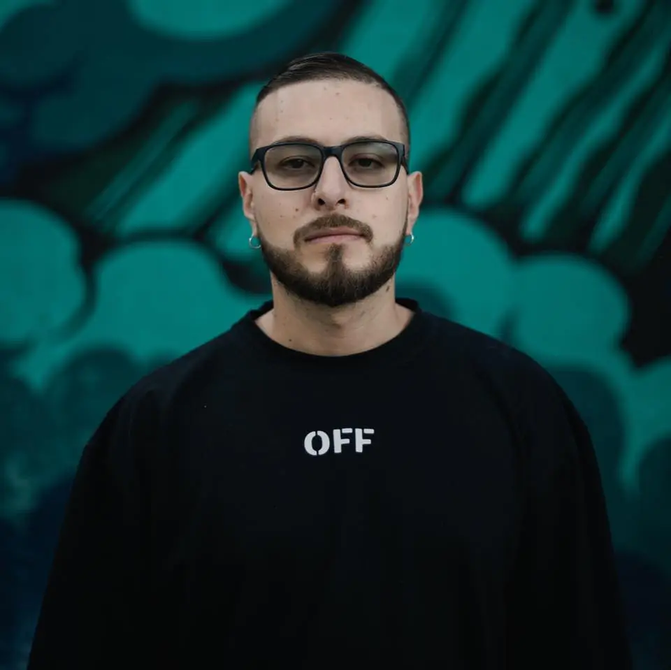 AFM with glasses wearing a casual off sweatshirt, looking directly at the camera with a neutral expression.