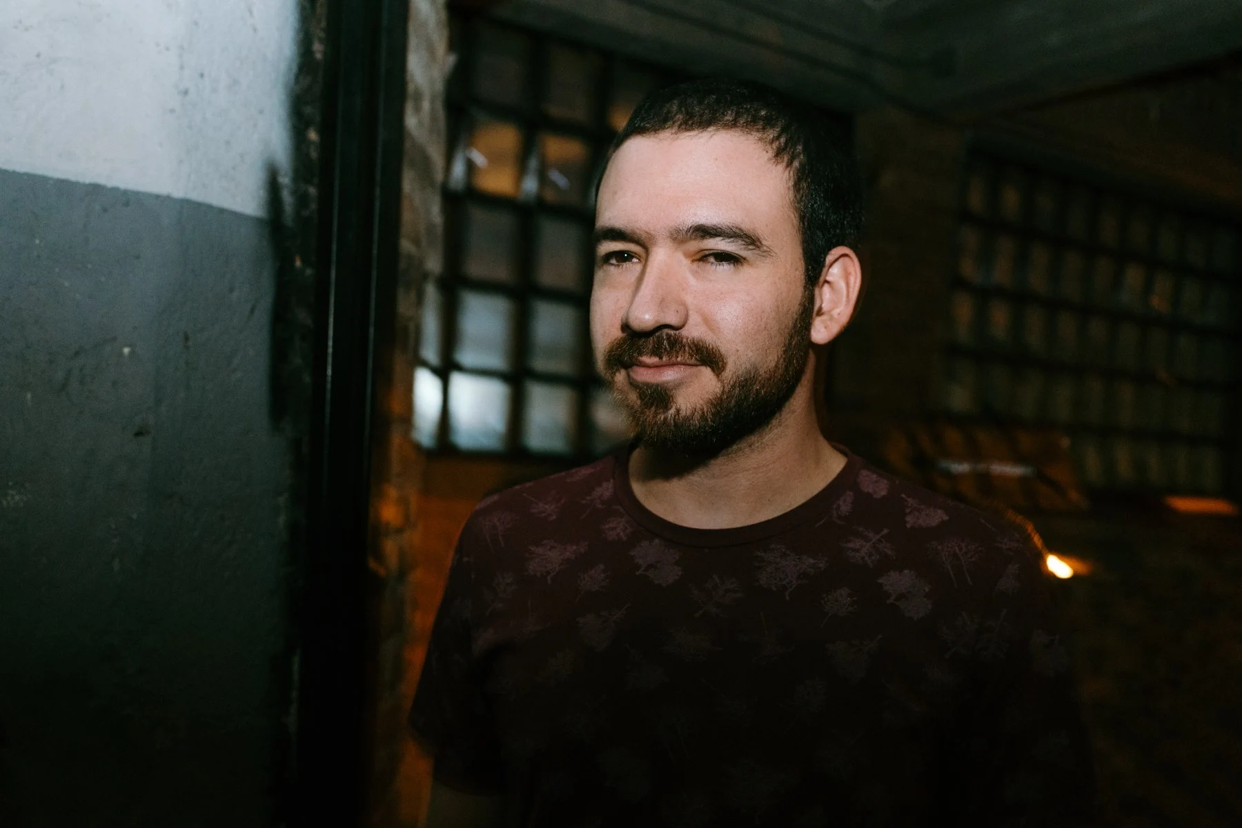 DCM in a red shirt stands in front of a door, looking directly at the camera.