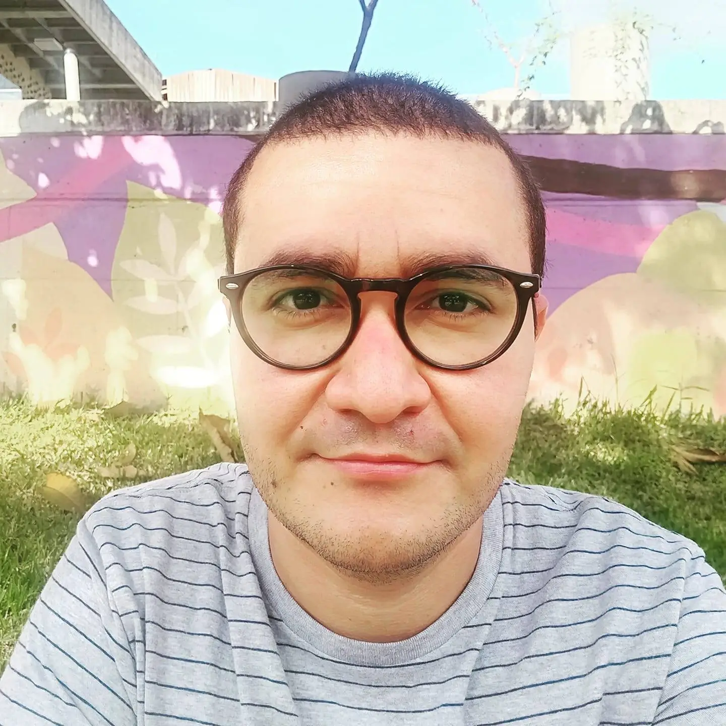 Douglas Fugazi wearing glasses and a striped shirt stands in front of a vibrant, colorful mural.