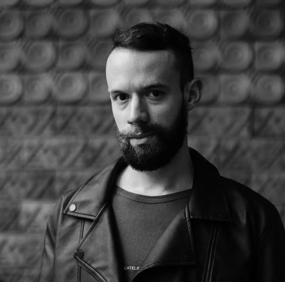 Insanity Circle with a beard wearing a leather jacket poses against a rustic brick wall backdrop.