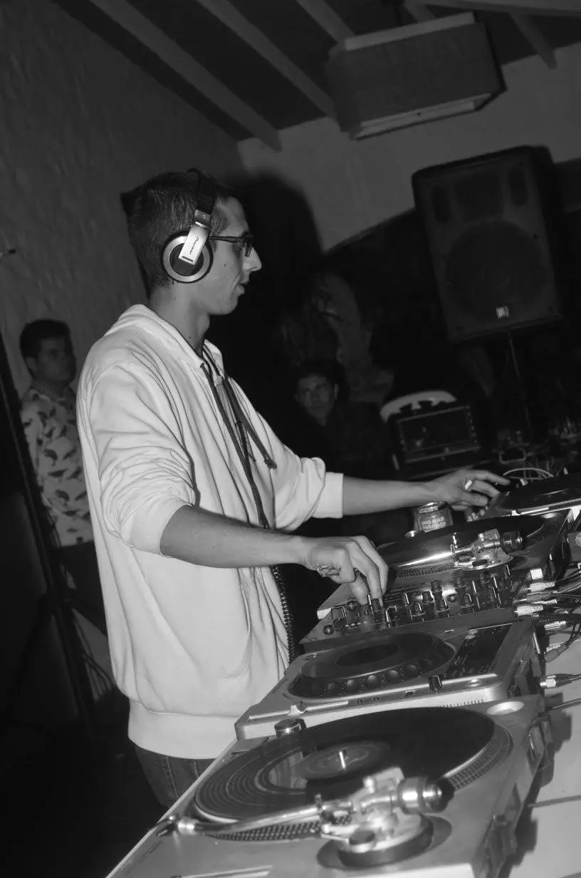 Joed Kleem skillfully mixing tracks, with turntables and sound equipment in a lively atmosphere.