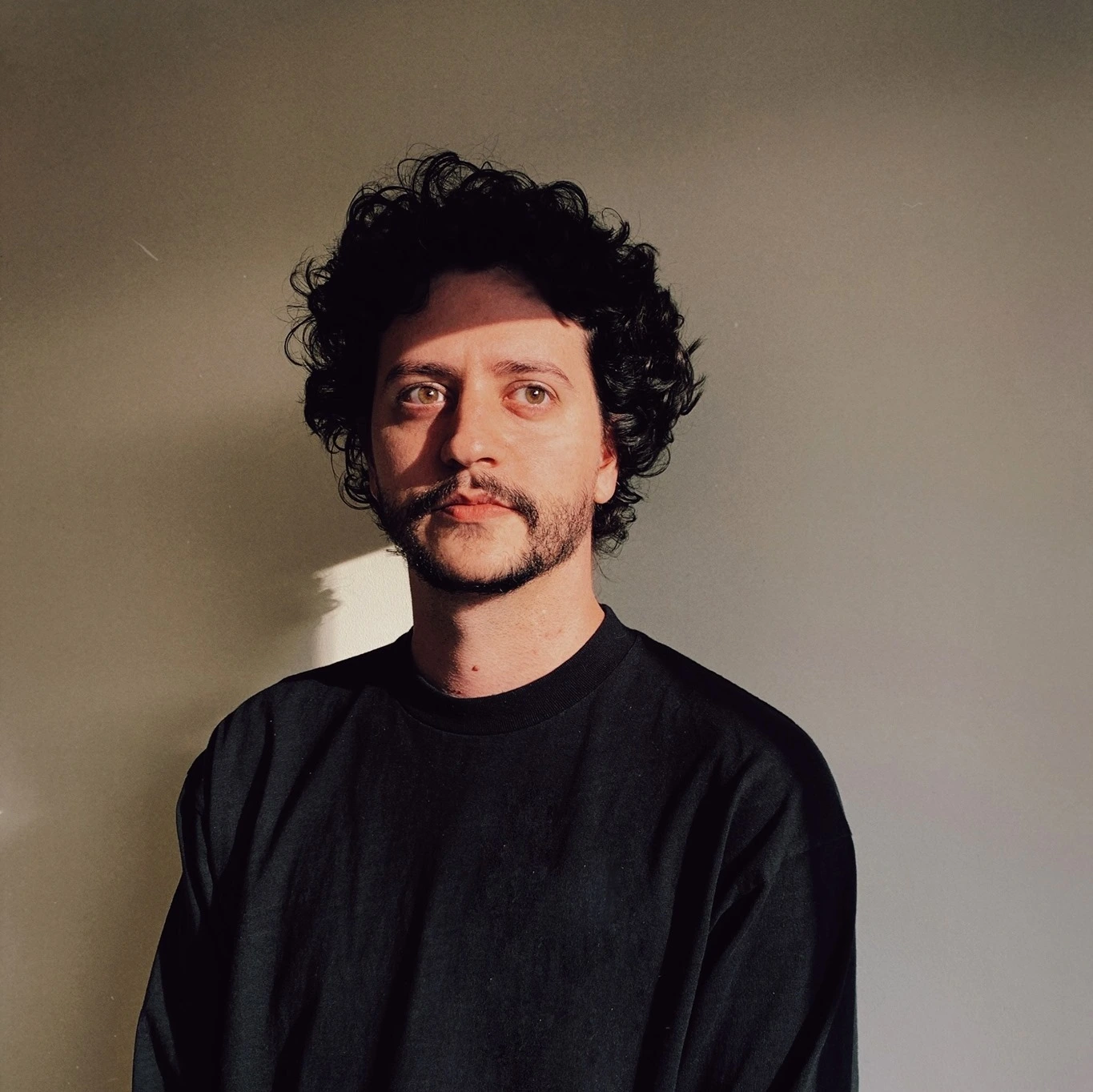 Merino curly hair wearing a black shirt, looking directly at the camera with a neutral expression.