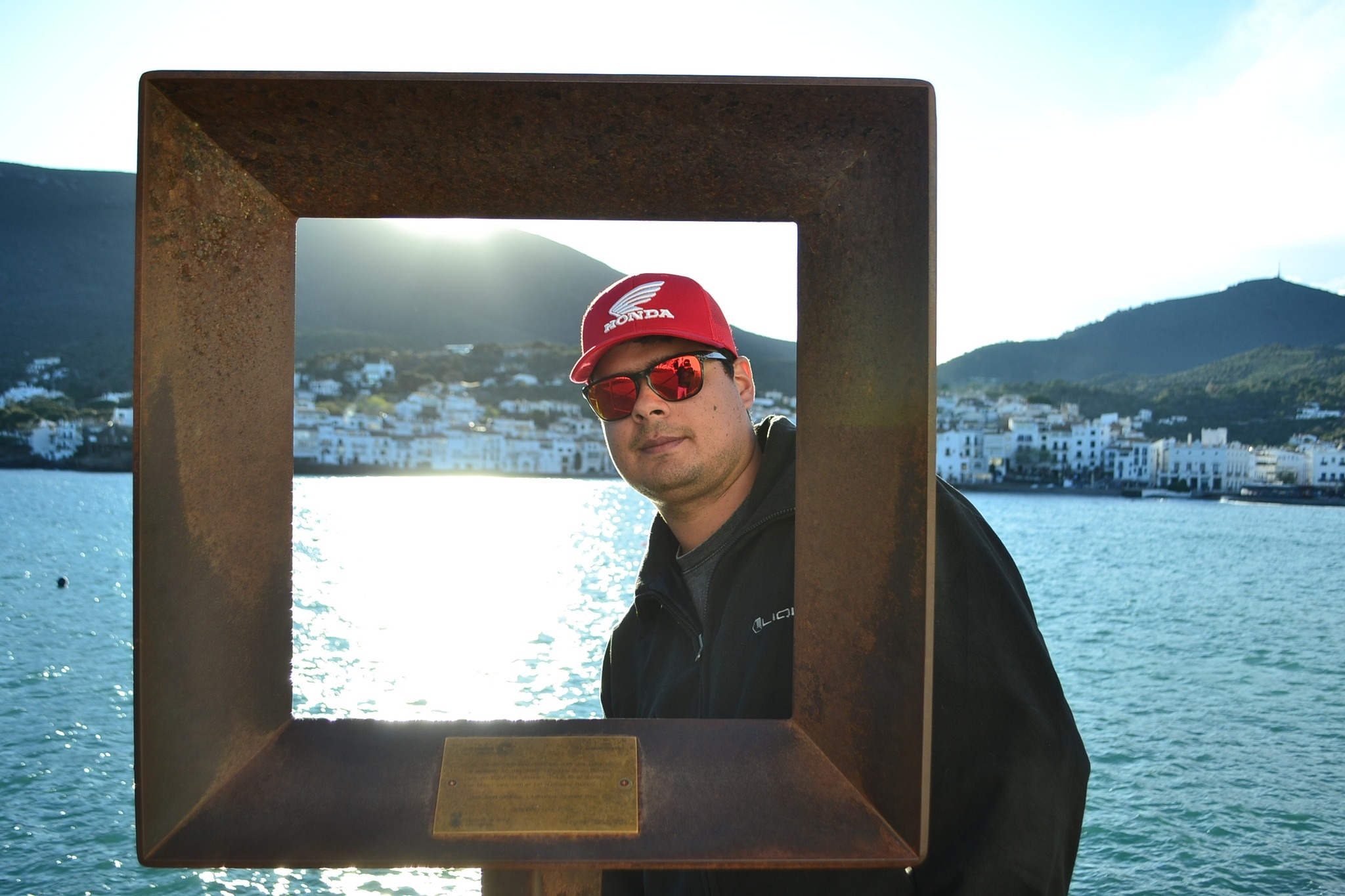 Miguel Duque wearing a red hat and sunglasses, smiling and standing outdoors in bright sunlight.