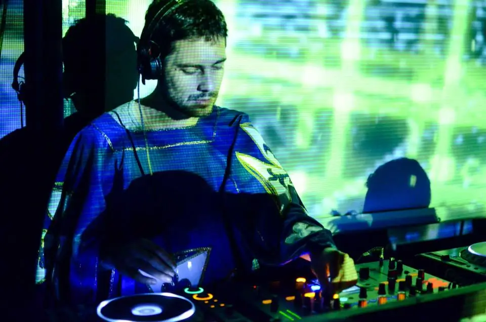 Morris in a blue shirt performing a DJ set, focused on mixing music at a lively event.